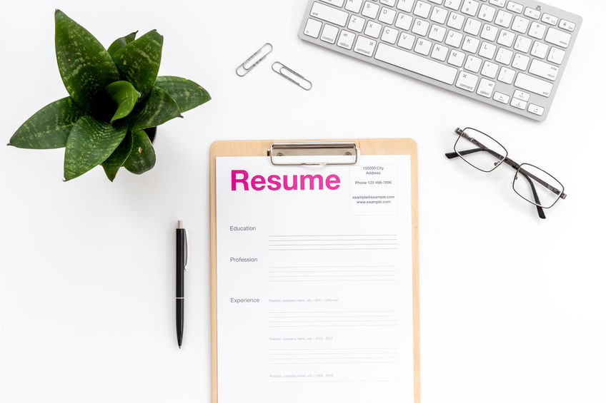 A neatly arranged desk with a resume on a clipboard, a keyboard, a potted plant, glasses, and a pen, all on a white background.
