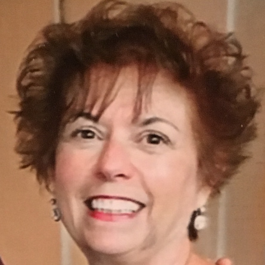 A portrait of a smiling elderly woman with short curly brown hair, wearing earrings and a subtle makeup.